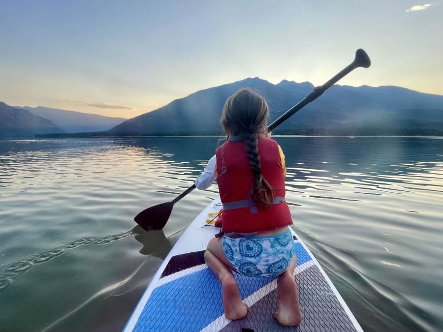 Amelie's daughter paddleboarding on a mountain lake at sunset