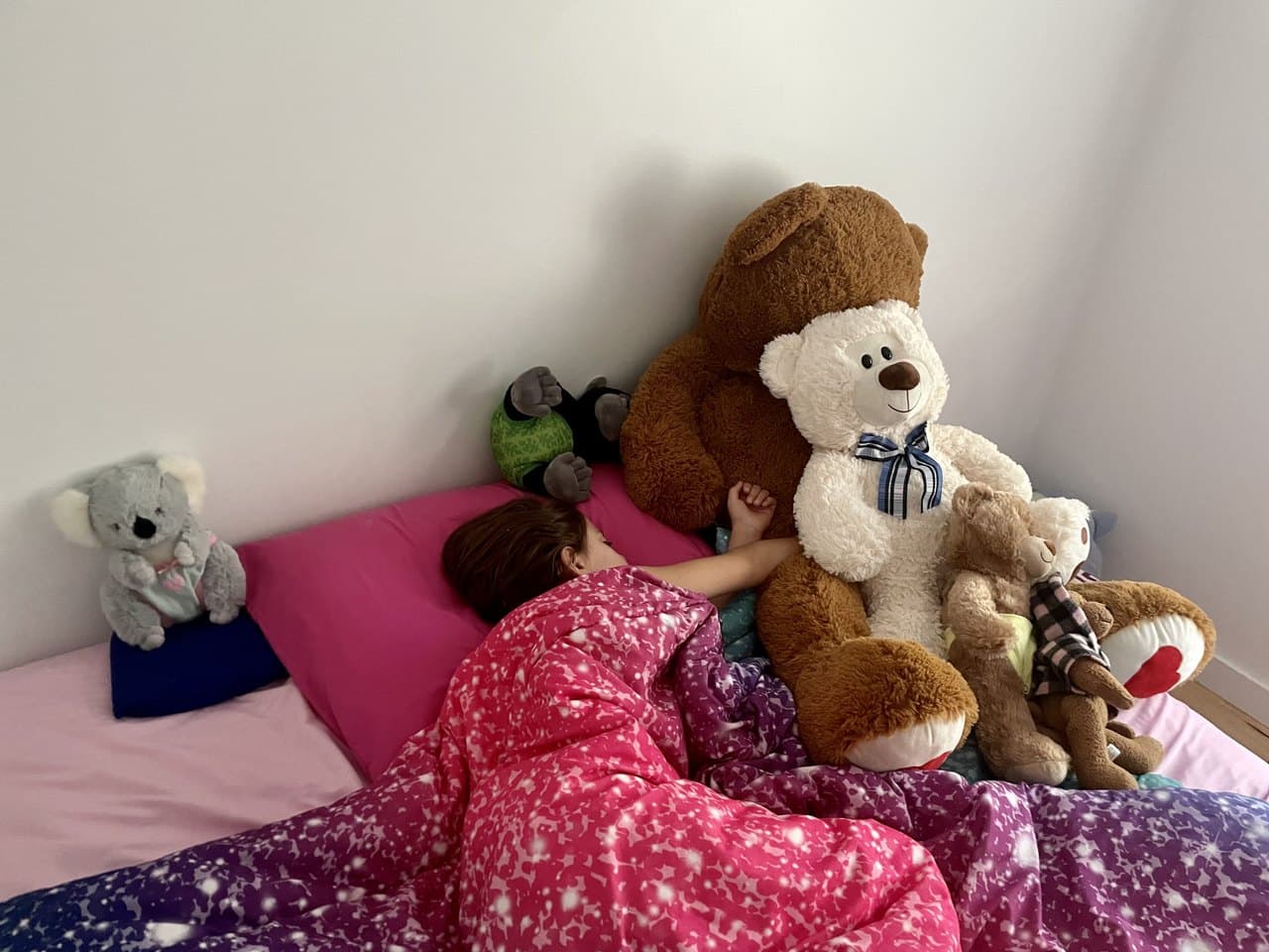 A young child fast asleep in bed surrounded by a pile of stuffed animals, mid-morning light