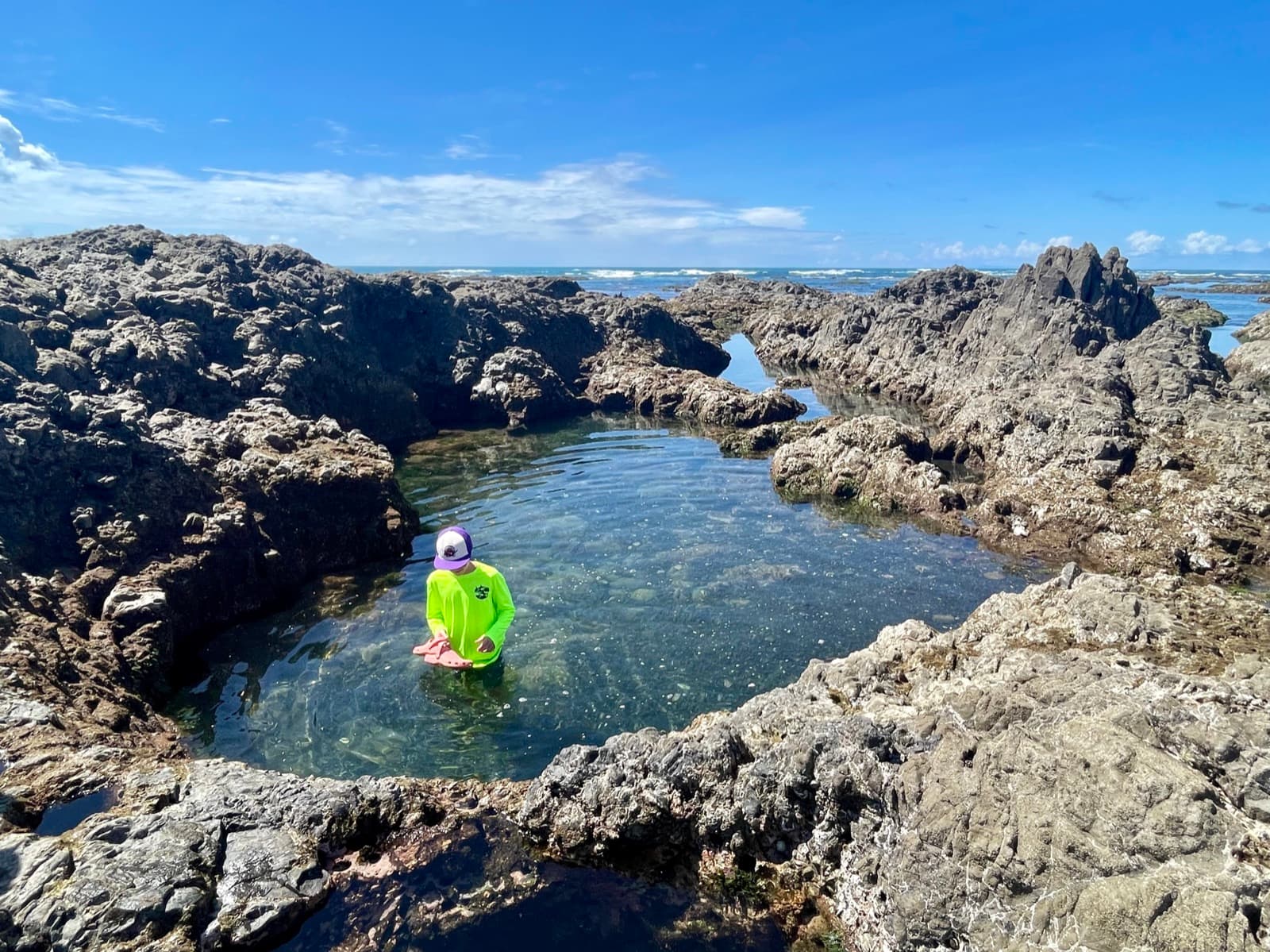 Child exploring a natural tidal rock pool surrounded by volcanic rocks and ocean waves