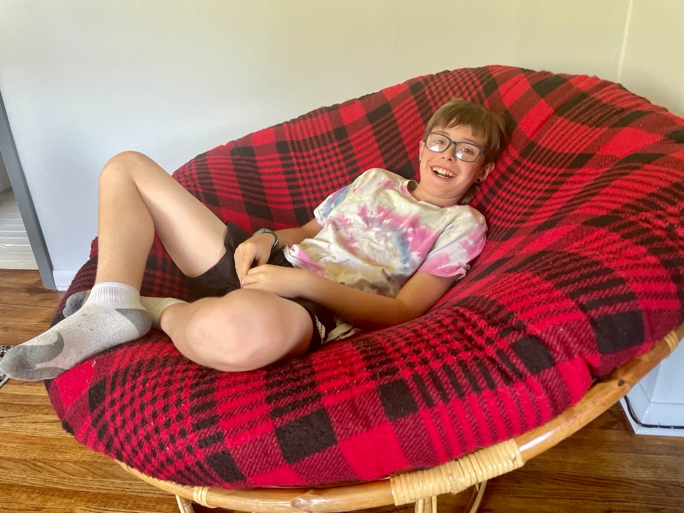 A child sprawled sideways in a big red papasan chair at home, relaxed and content with nothing in particular to do