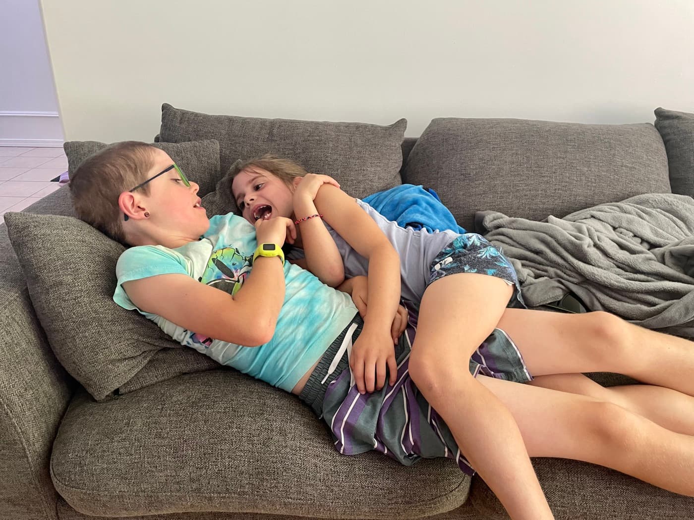 Two siblings piled together on the couch at home, tangled up and laughing, having turned an empty afternoon into their own game