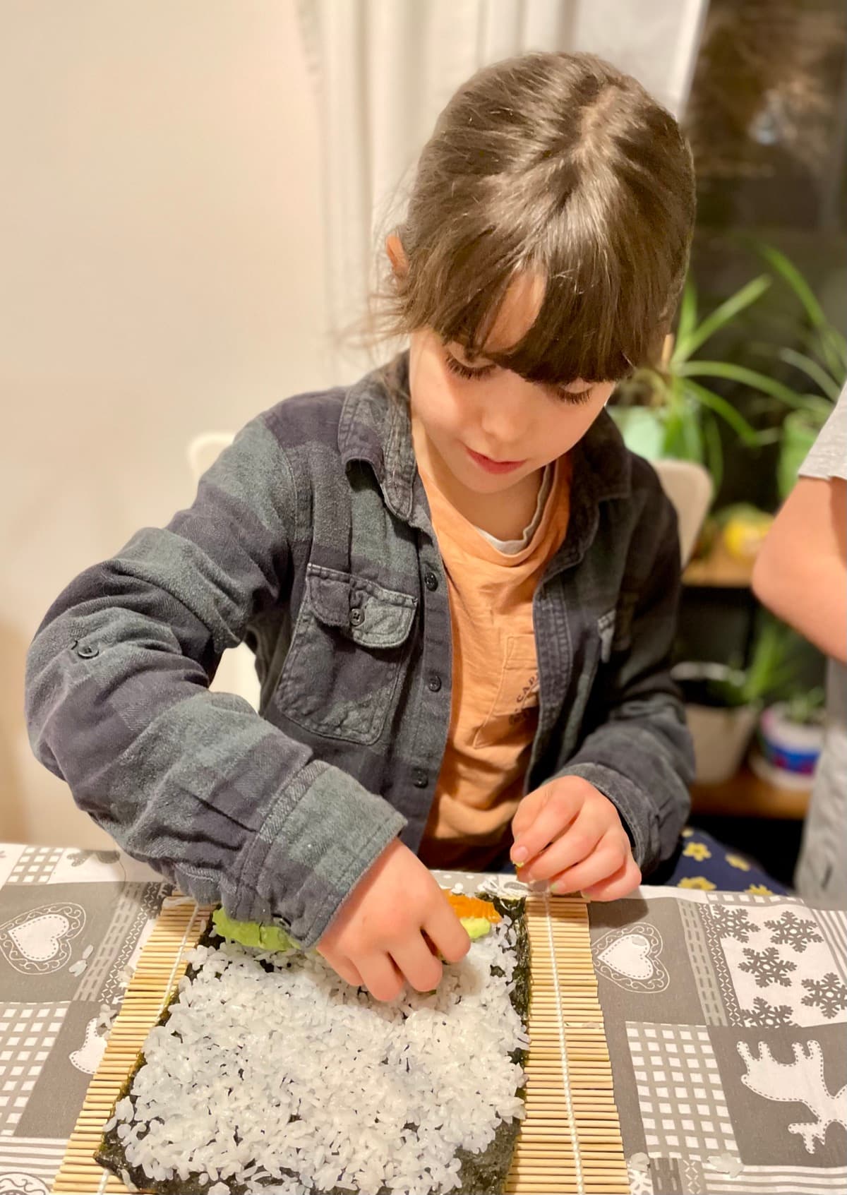 Child carefully assembling sushi with a bamboo rolling mat at the kitchen table