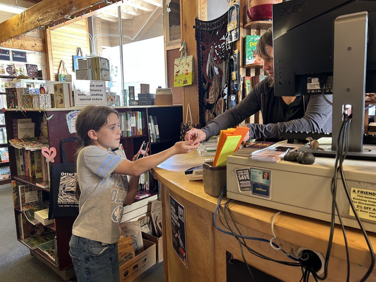 A child paying at a bookstore counter on her own, handling her own transaction and talking to the cashier