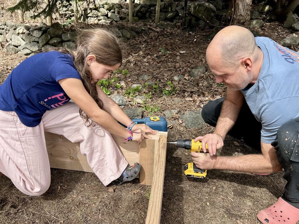 A girl and her dad building a wooden frame with a drill