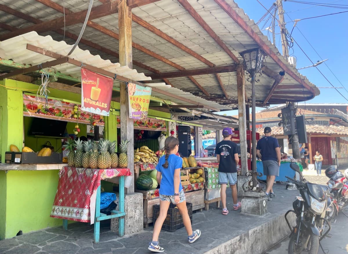 Julia and Zach walking past a colourful fruit stand in a walkable town
