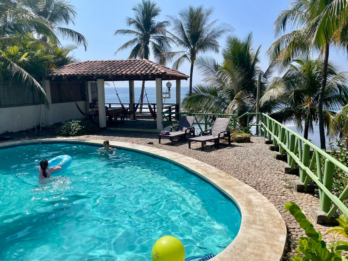 Kids swimming in a beachside pool in El Zonte, El Salvador, palm trees and ocean in the background