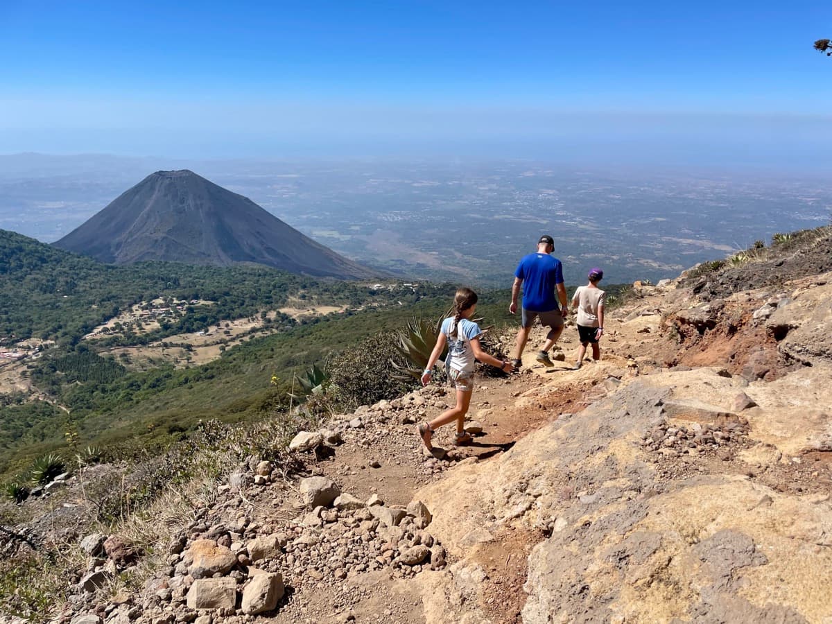 Family hiking down a volcano trail with a second volcano rising in the distance
