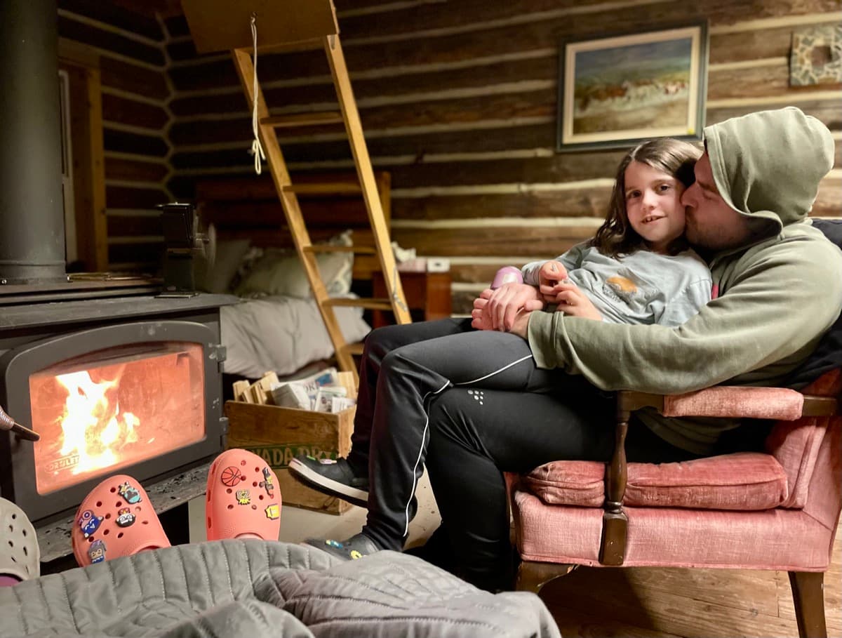 Dad and daughter sharing a quiet moment by the wood stove in a cozy cabin