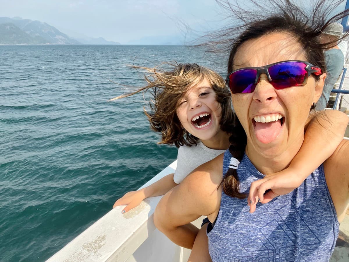 Mom and child laughing together on a boat ride, wind blowing through their hair