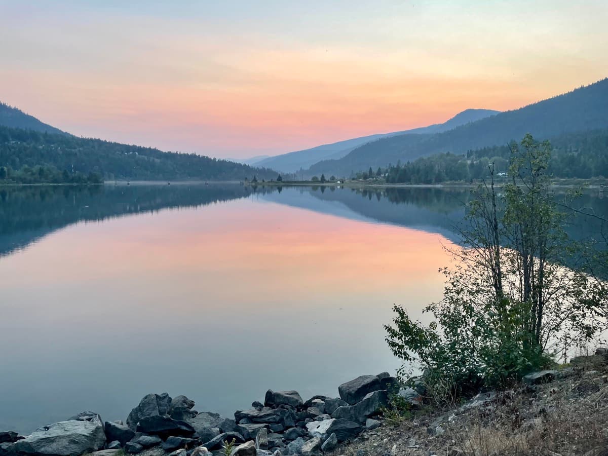 Calm lake at sunset with mountains in the background, a peaceful moment outdoors