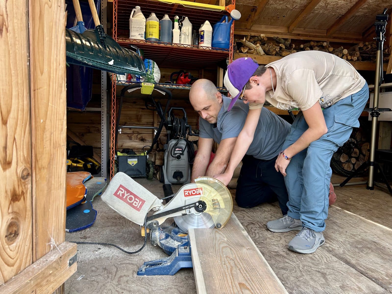Dad and son working a mitre saw together in the workshop, cutting lumber for a real project, the kind of hands-on engineering kids remember for life