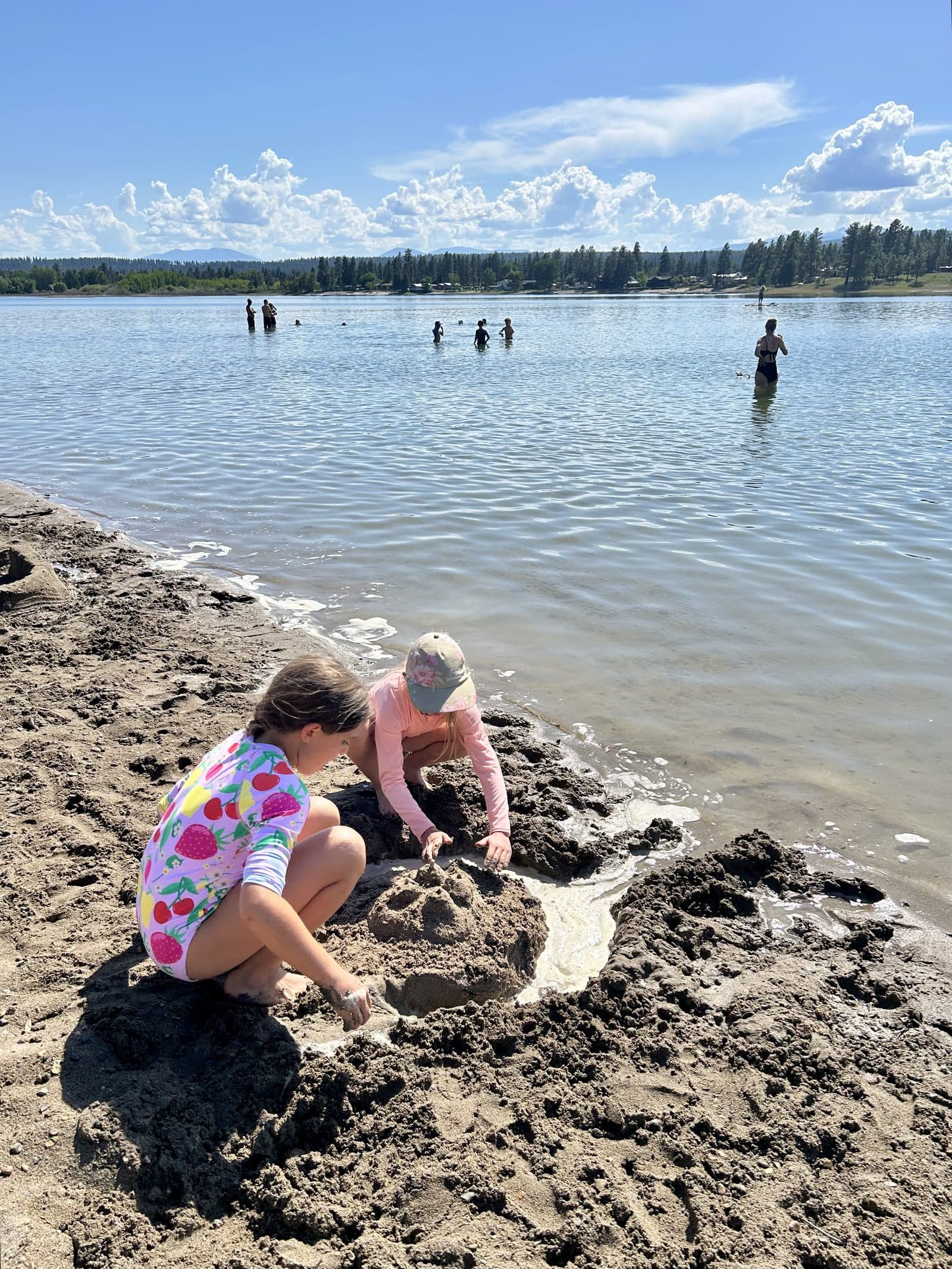 Two kids shaping a sand channel and dam at the edge of a lake, water flowing through the structure they built