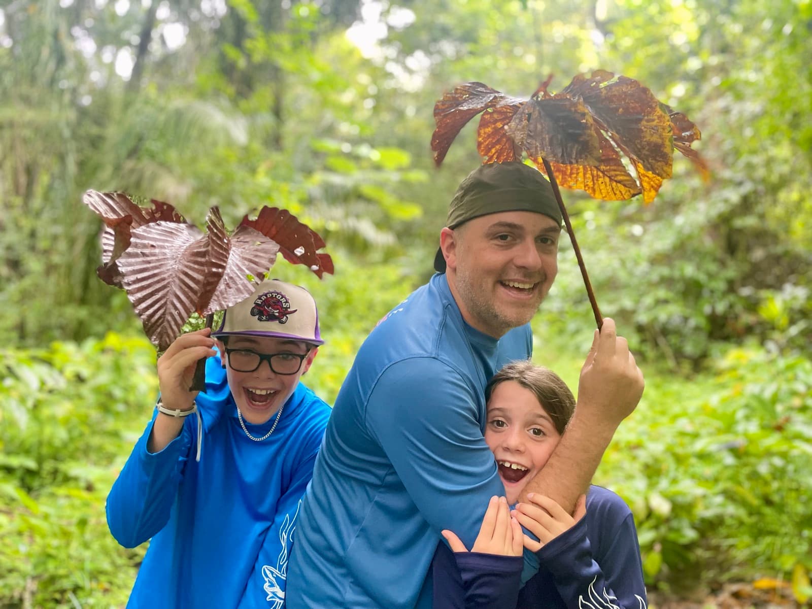 Family laughing together while holding giant tropical leaves over their heads in a lush green forest
