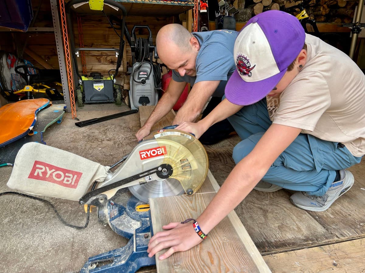 Zach measuring and cutting wood with dad at the miter saw in the garage