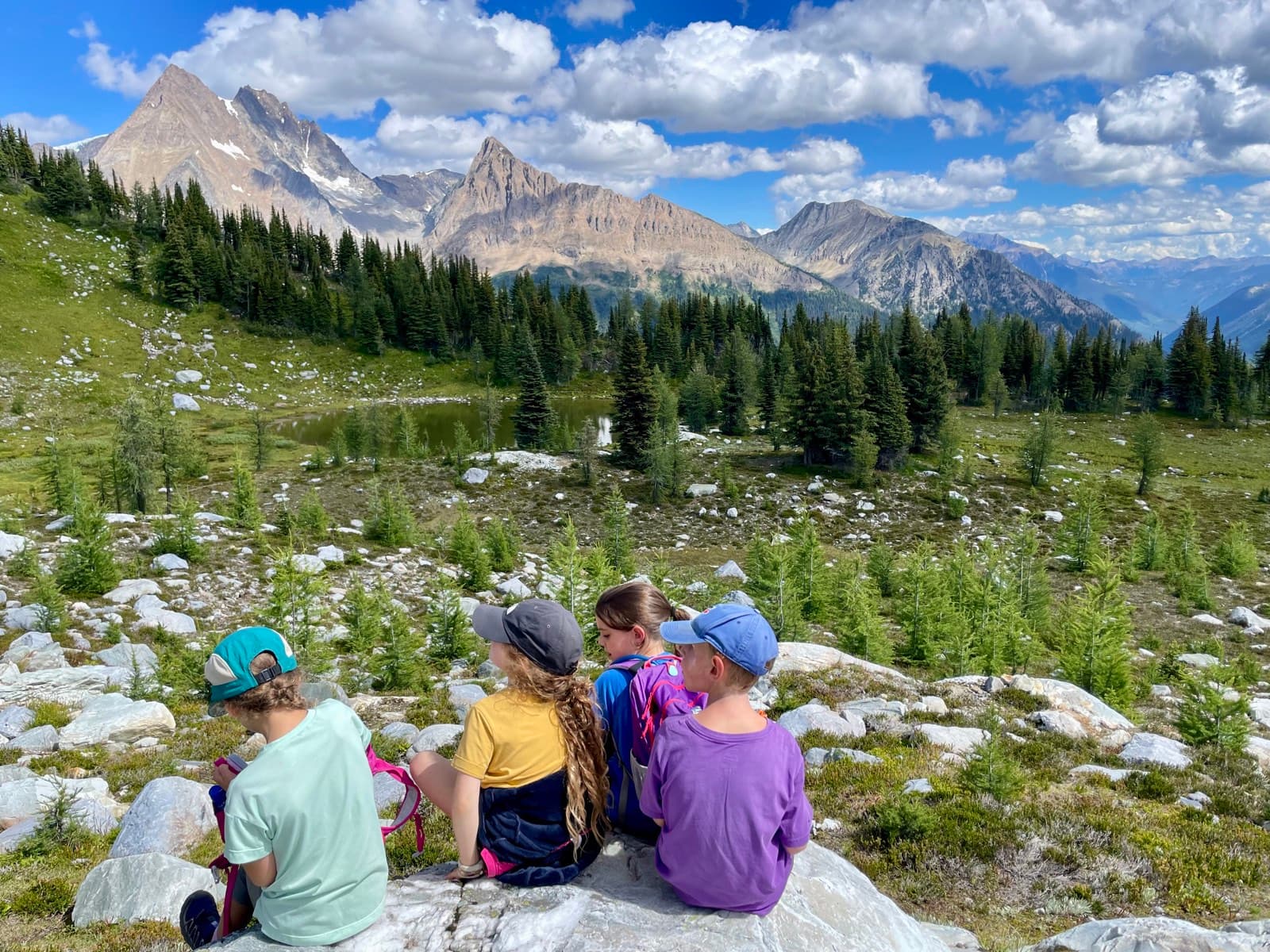 Four kids sitting together on a rock looking out across a wide mountain valley, the quiet kind of shared moment real friendships are made of