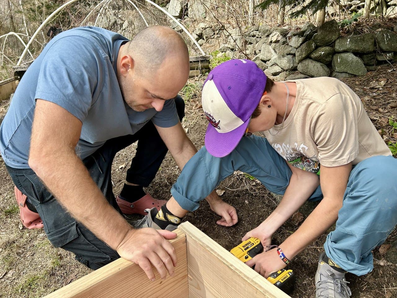 A parent and a middle schooler building a garden box together outdoors, the tween using a drill while the parent steadies the wood