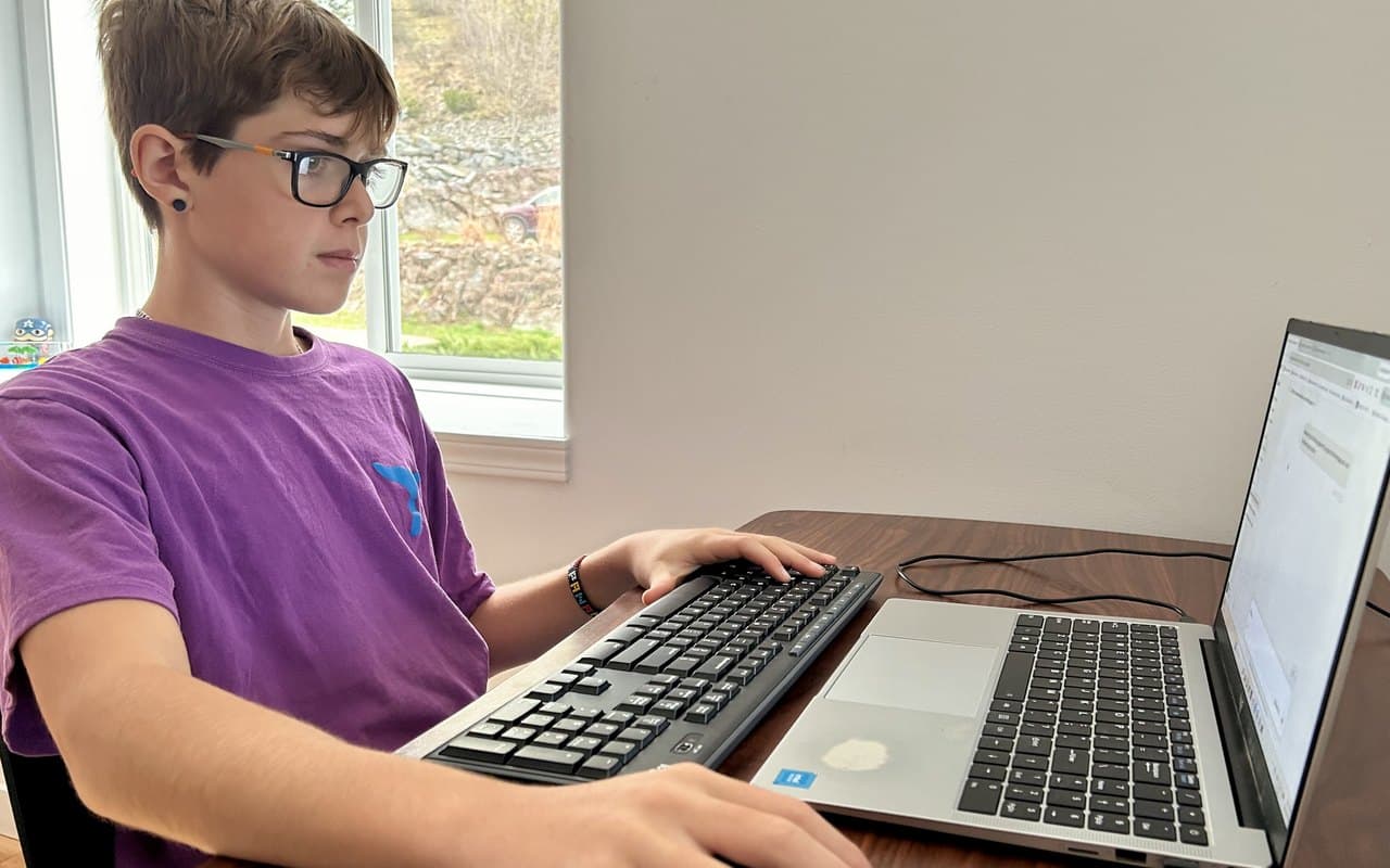 A homeschooled middle schooler working independently at a laptop with a keyboard and mouse, focused and in charge of his own learning