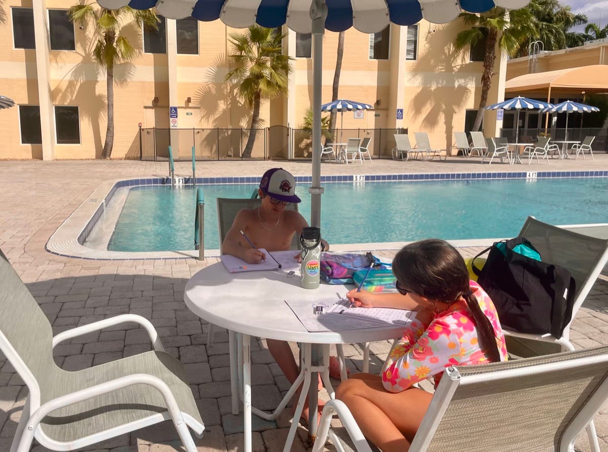 Two kids doing schoolwork by the pool in Florida, learning doesn’t need a desk