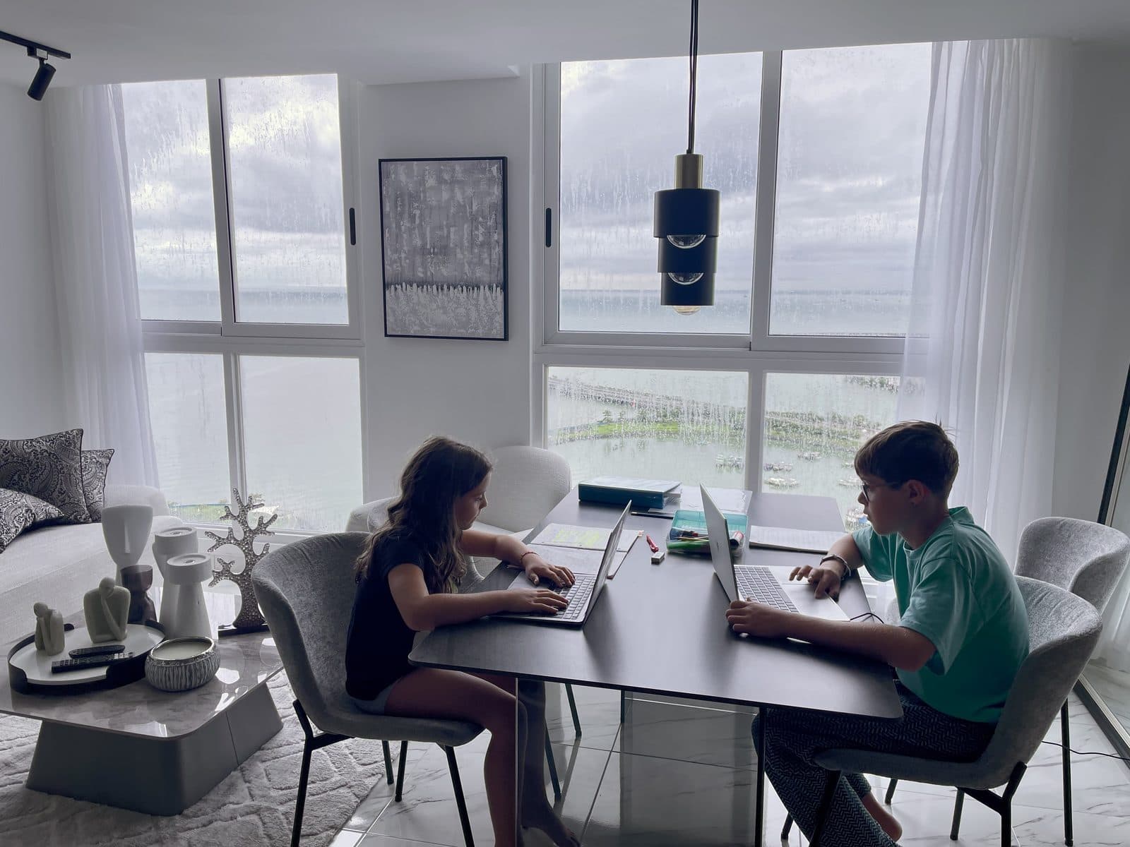 Zach and Julia working on their laptops at a dining table with ocean views, creating videos and digital projects together