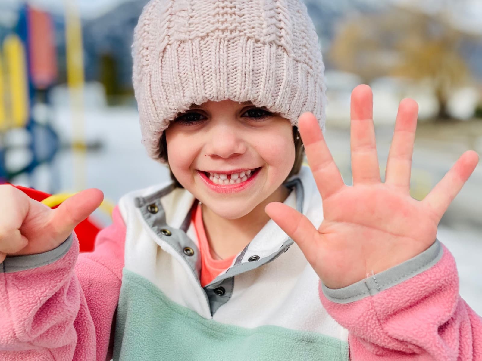 Young girl grinning at the camera with hands outstretched at a playground, pure kindergarten joy