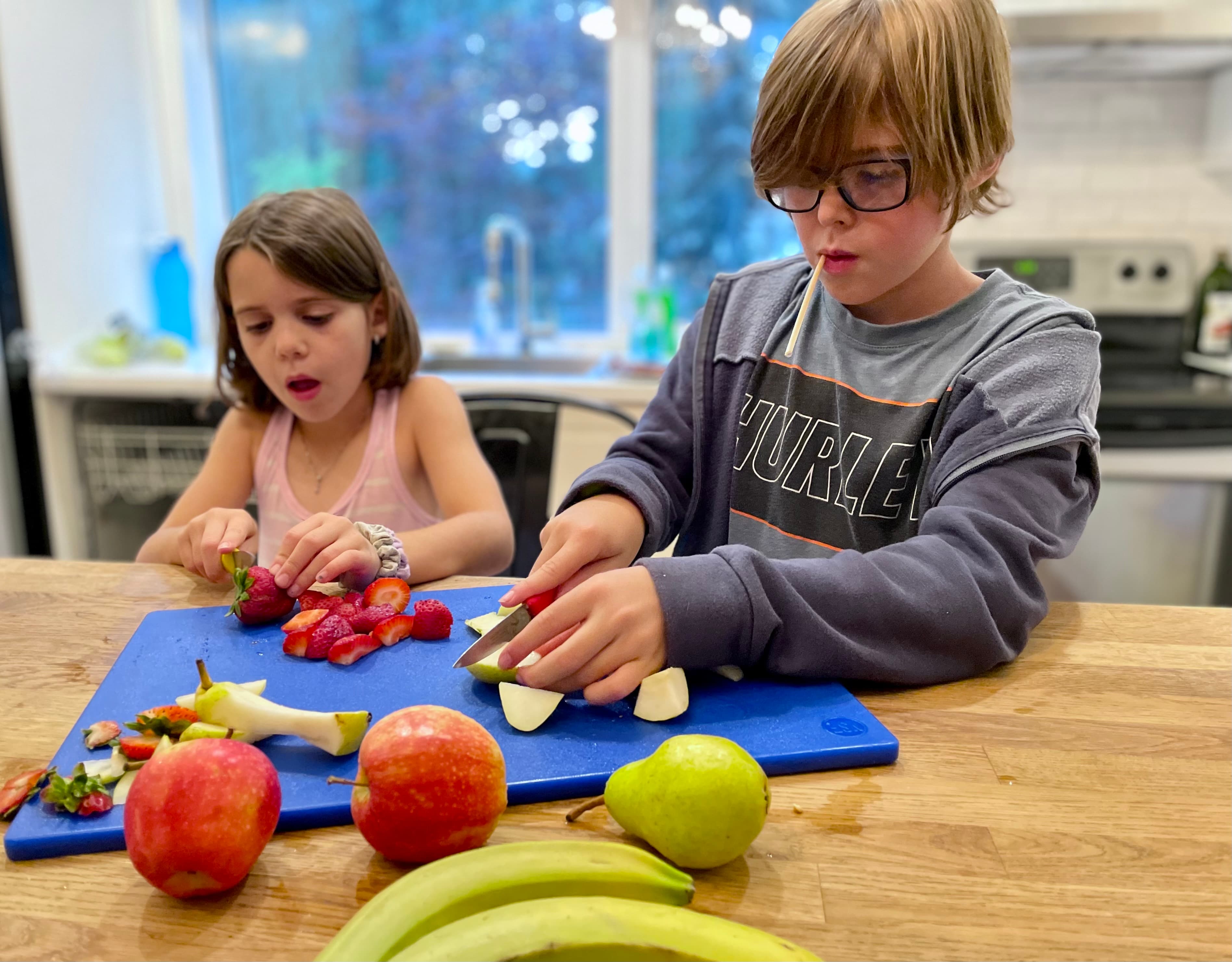 Two kids chopping fruit together at the kitchen counter