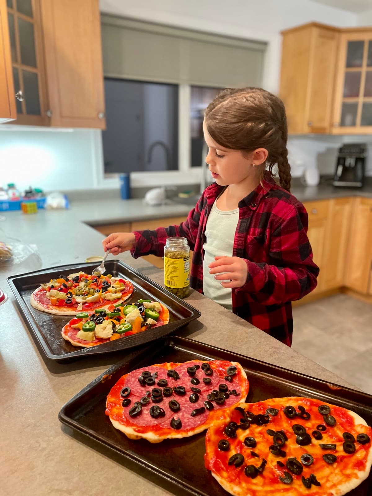 Julia carefully topping homemade pizzas in the kitchen: olives, peppers, and her own combinations