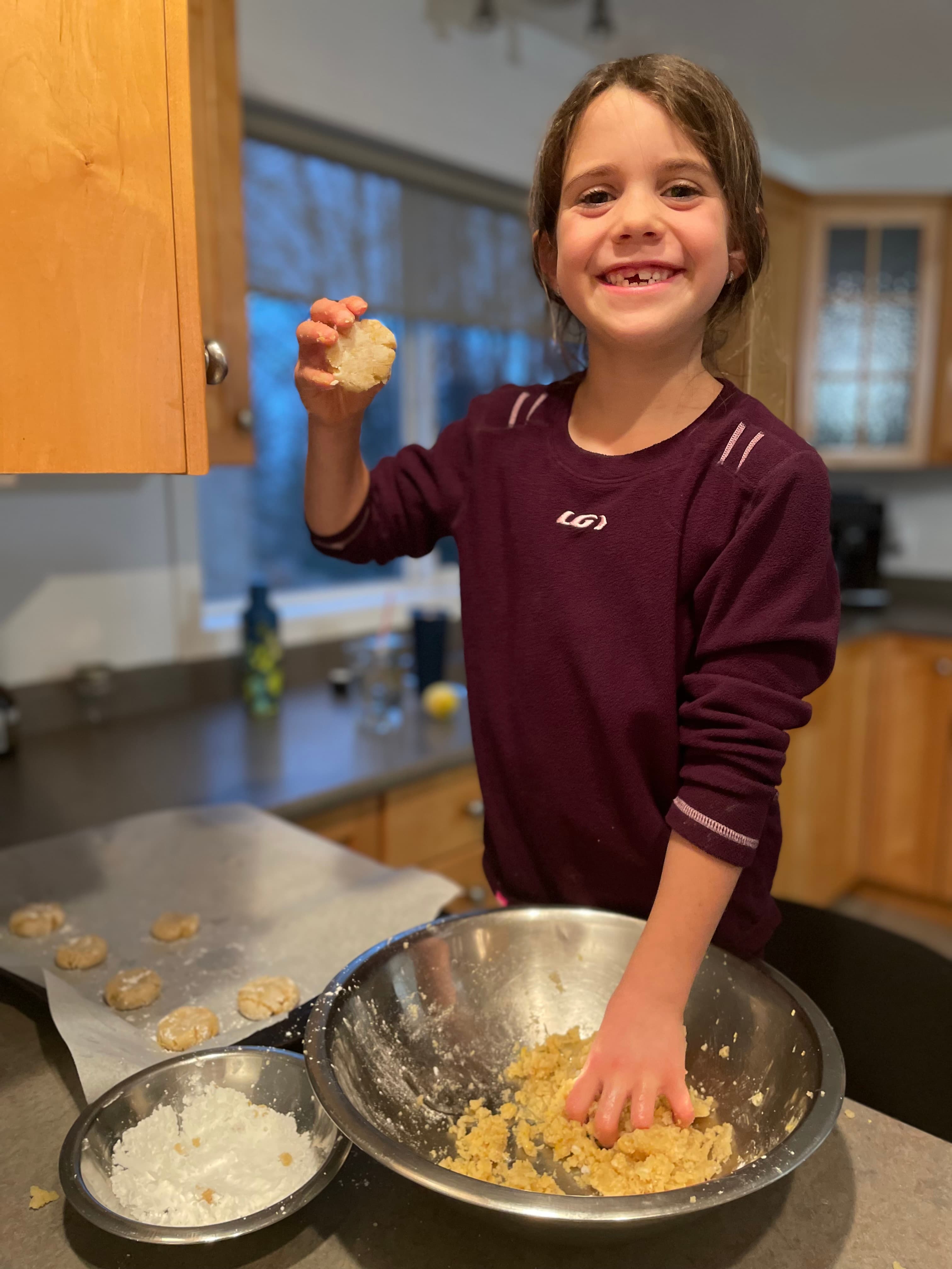 Child smiling proudly while shaping cookie dough in the kitchen