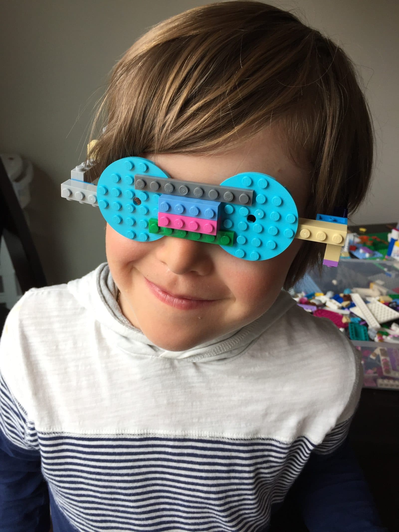 Kid wearing wearable LEGO glasses he designed and built from regular bricks, blue lenses and a multicolored bridge across the nose