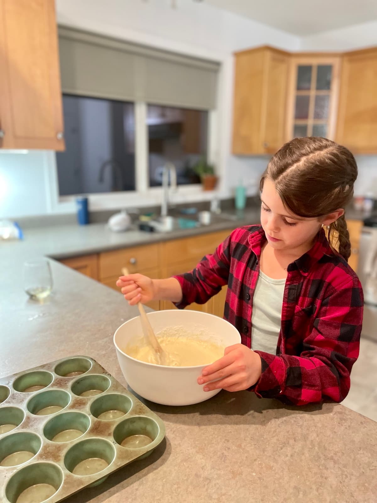 Julia stirring muffin batter in a big bowl with a muffin tin ready beside her