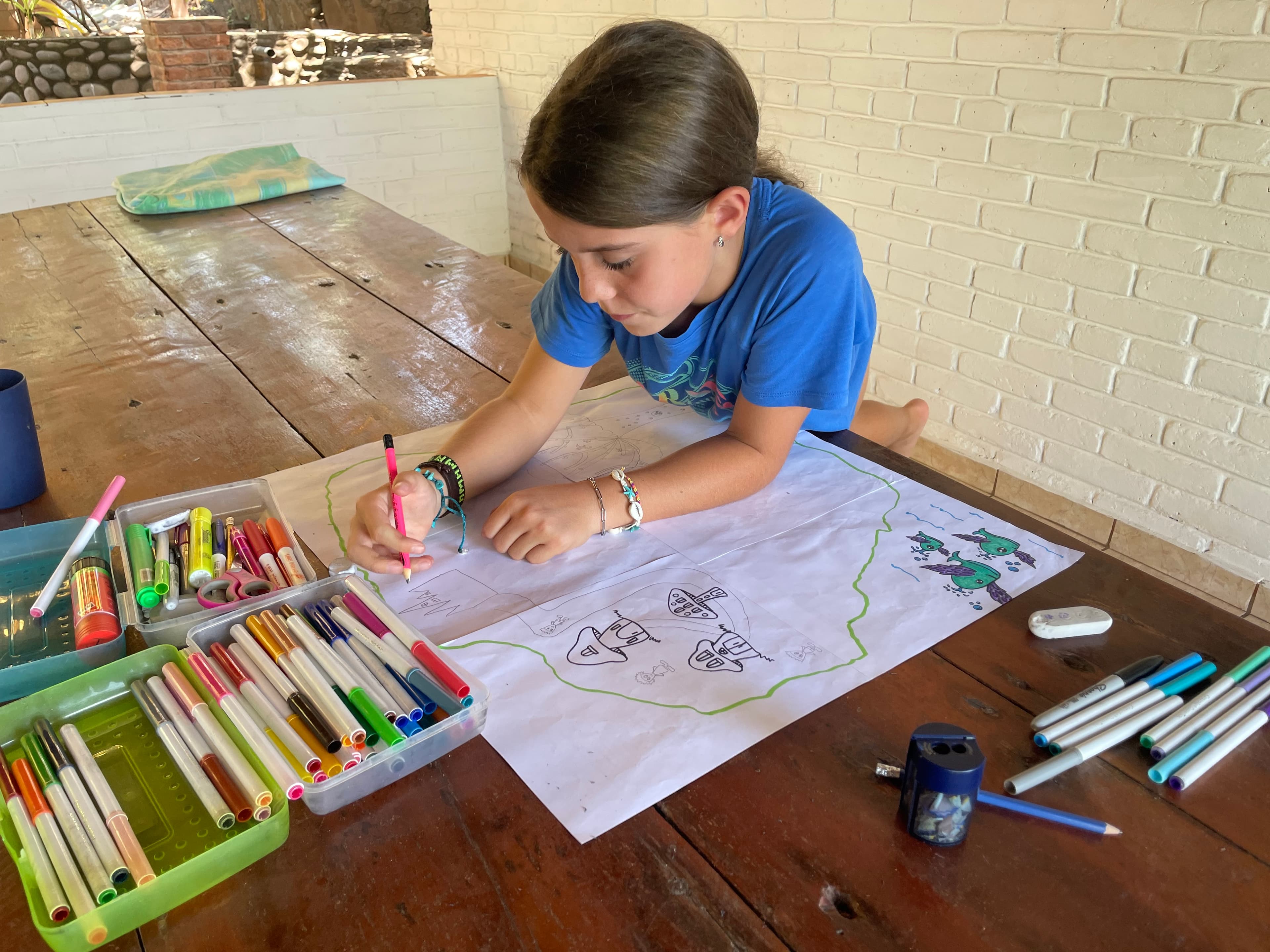 Child drawing a detailed map with coloured markers at a wooden table