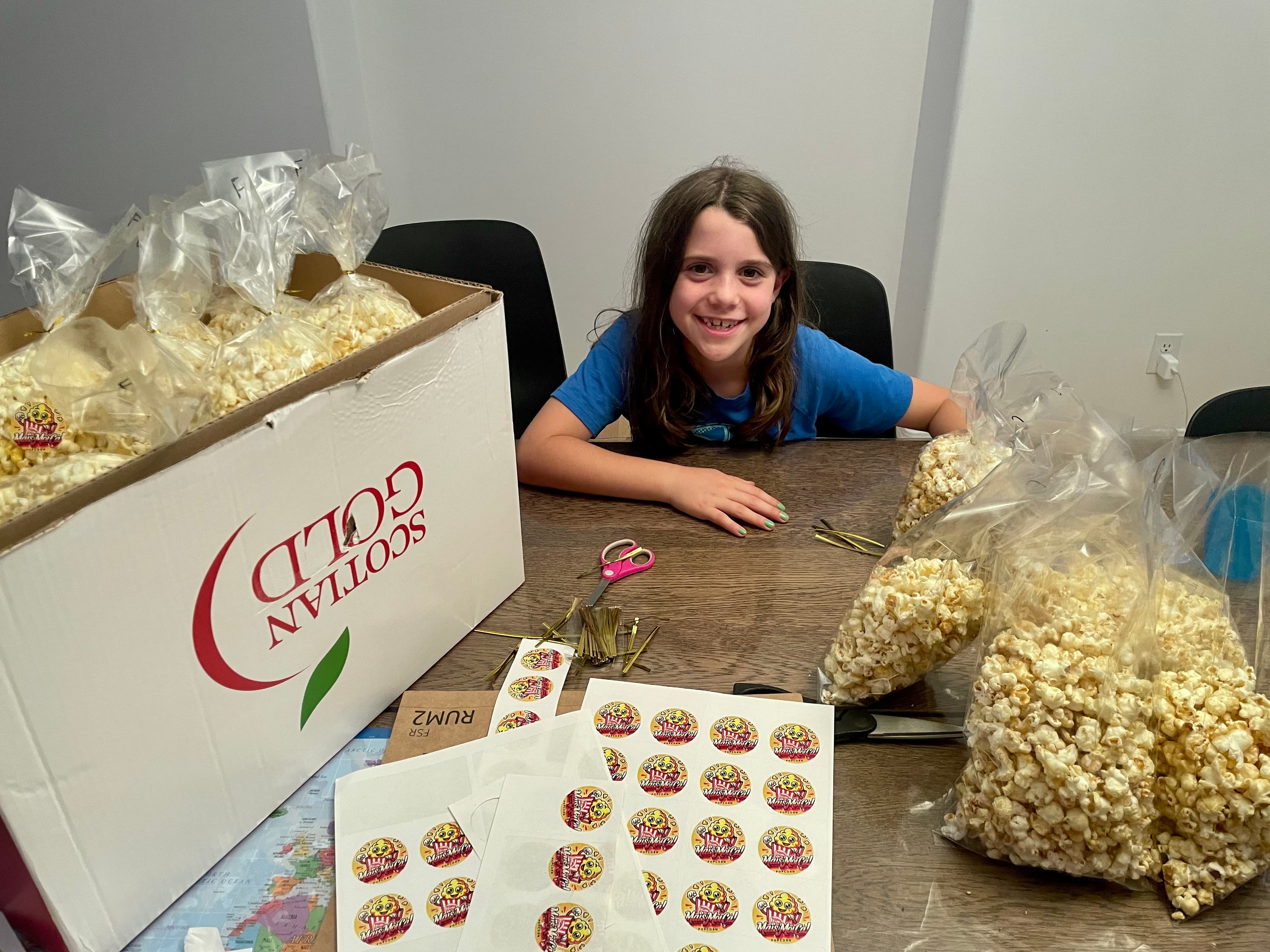 Girl proudly packaging popcorn bags with custom stickers to sell at a fair