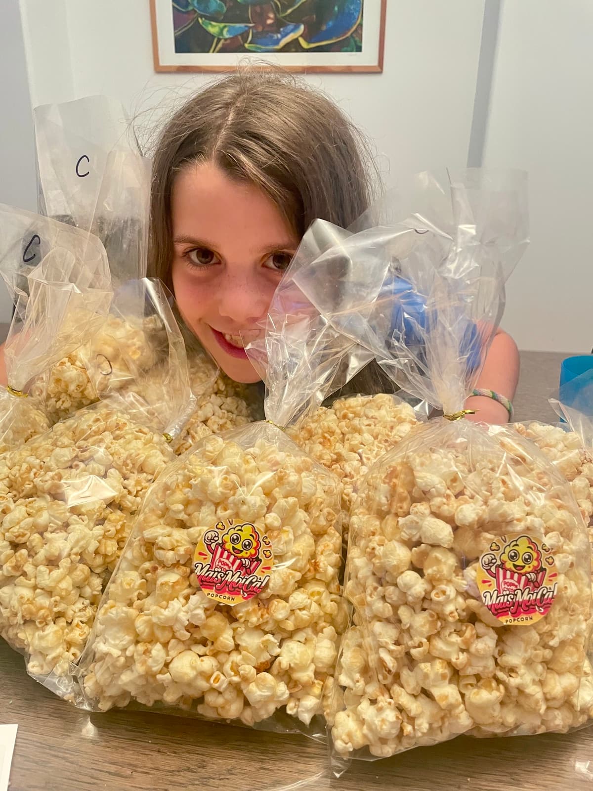 My daughter surrounded by bags of homemade popcorn with her own branded stickers, her real business