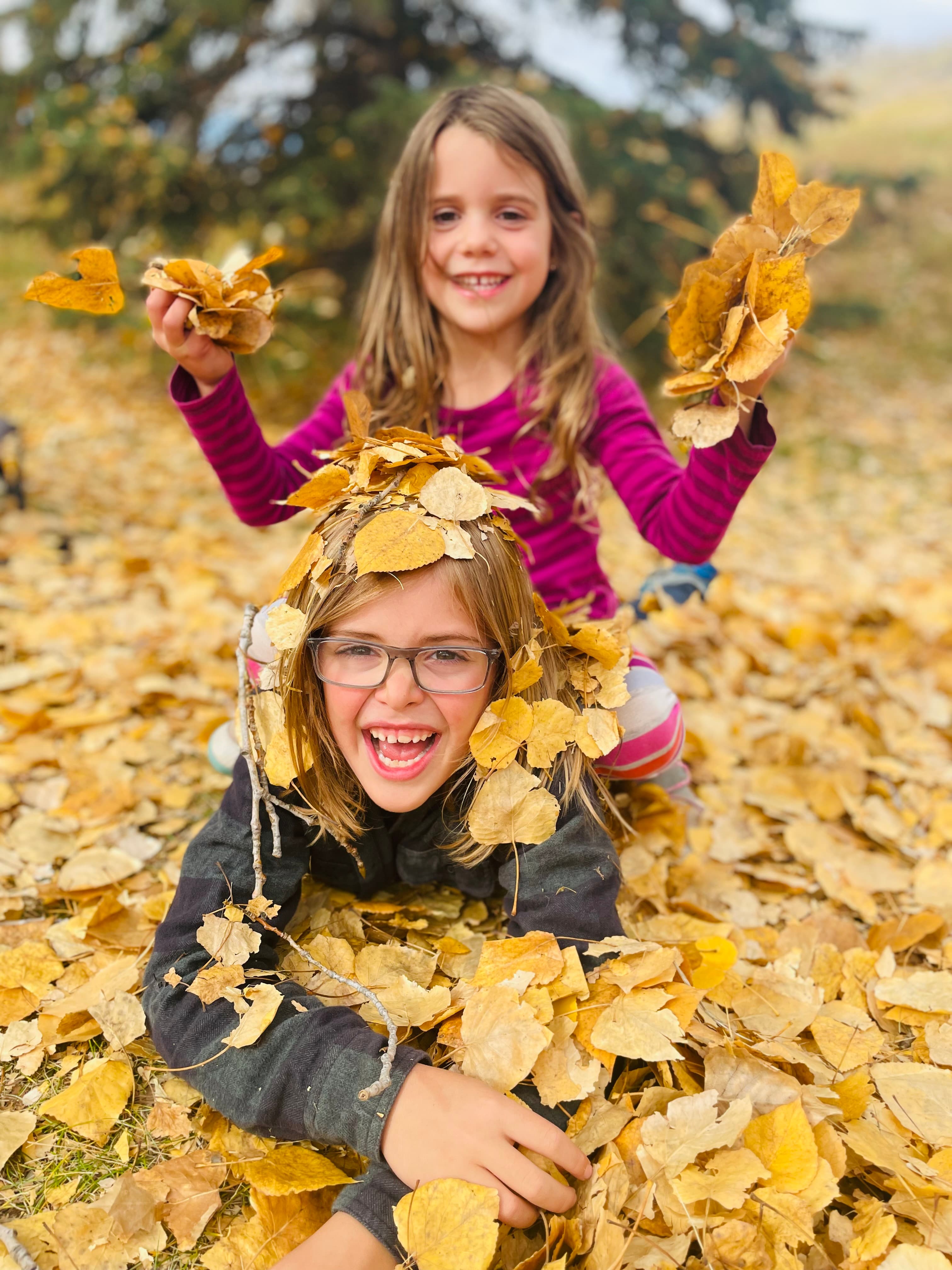 Two kids laughing and playing in a pile of golden autumn leaves