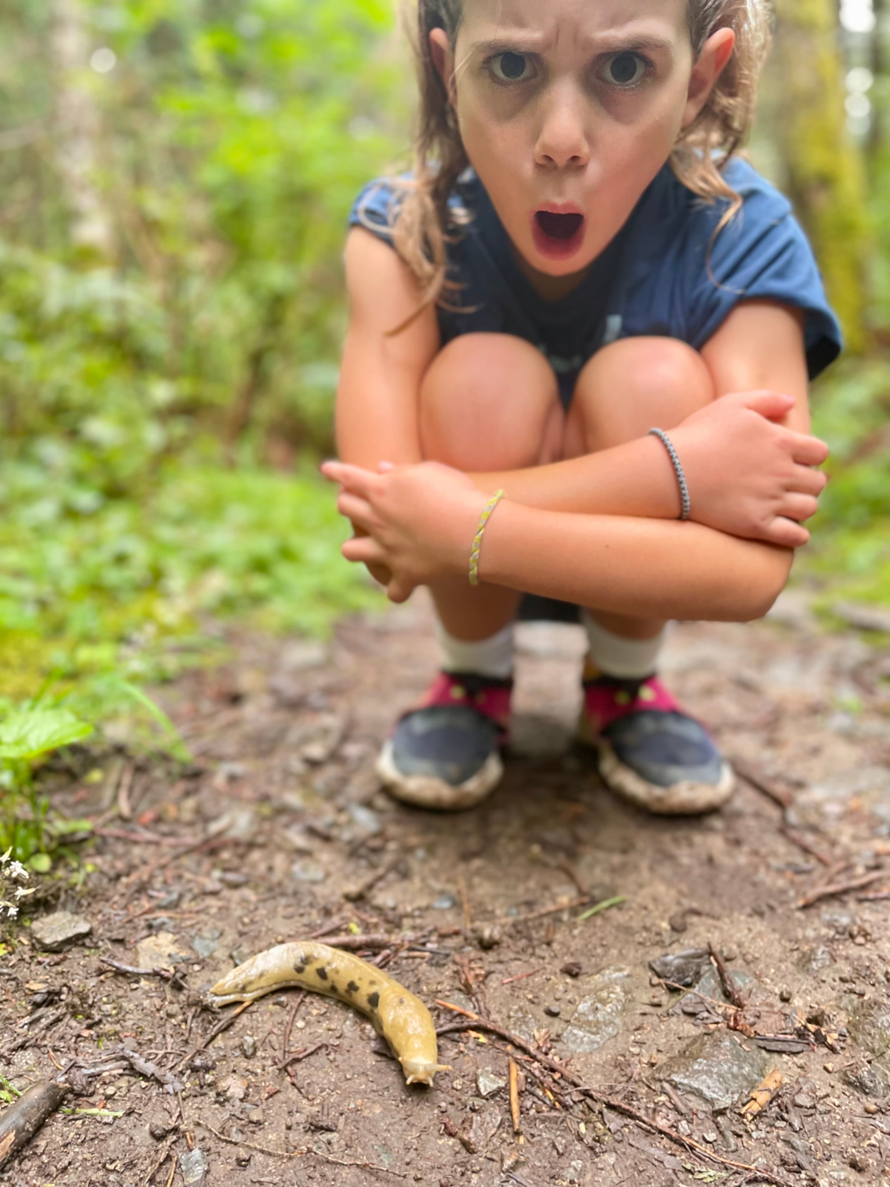 Child crouching down in amazement discovering a banana slug on a forest trail