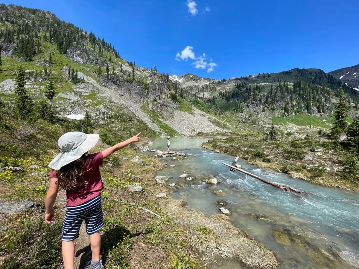 Girl pointing at a mountain stream with rocks and flowing water