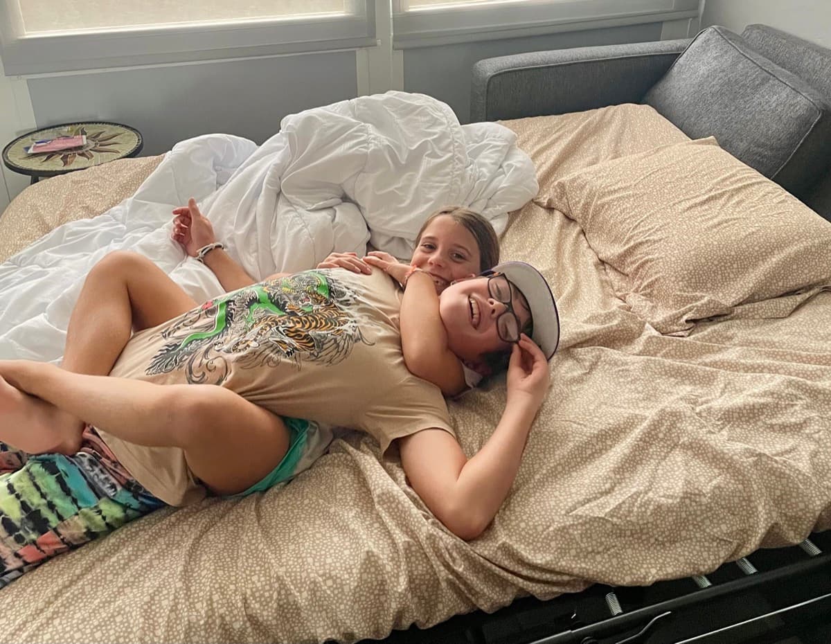 Zach and Julia relaxing on a bed in a rental, just living life with minimal stuff