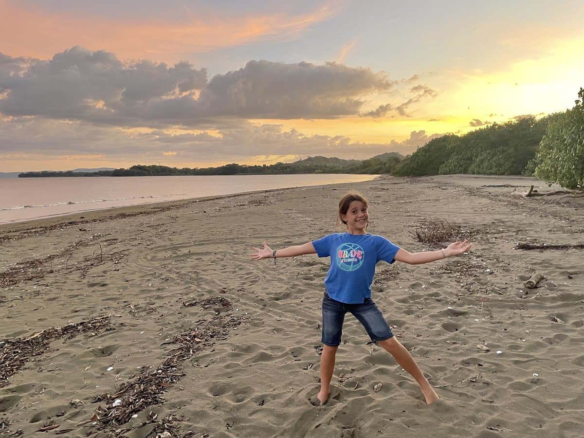 Julia with arms wide open on a beach at sunset, pure and unstructured joy