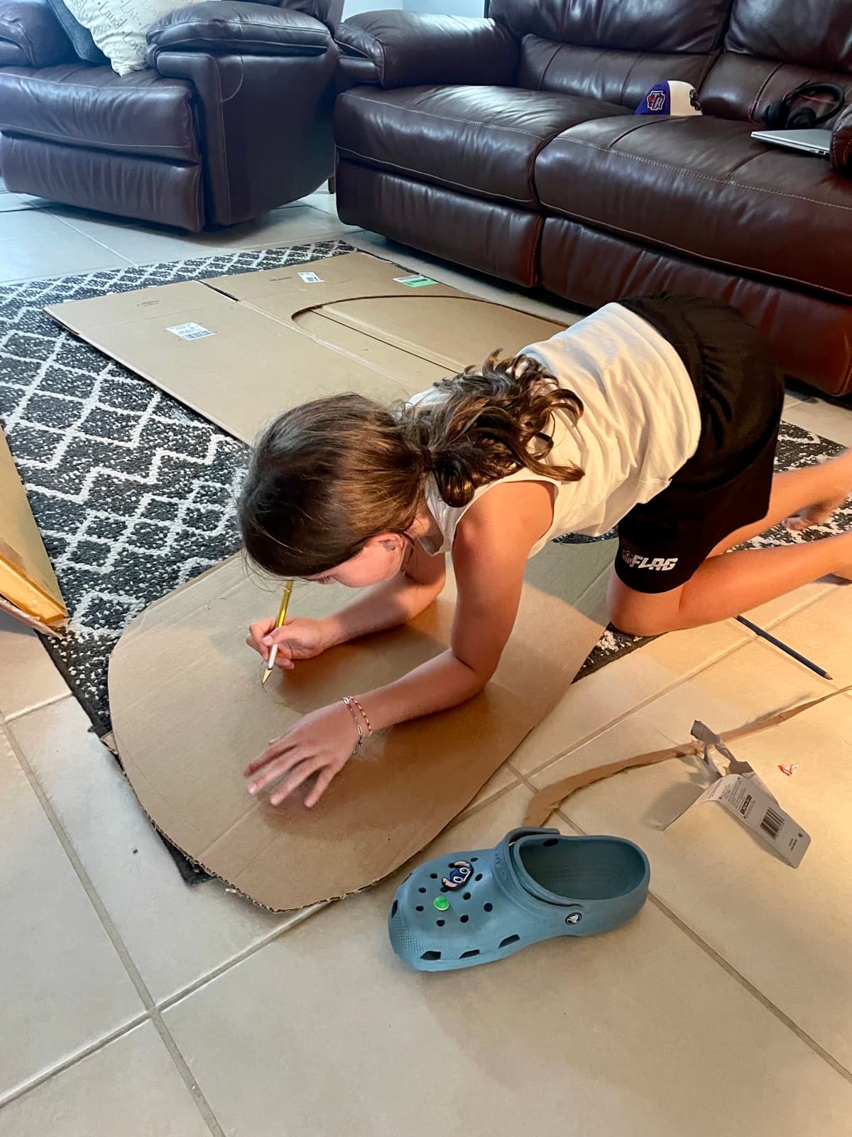 Julia on the floor drawing and cutting a giant cardboard Croc shape, designing her homemade Halloween costume from scratch