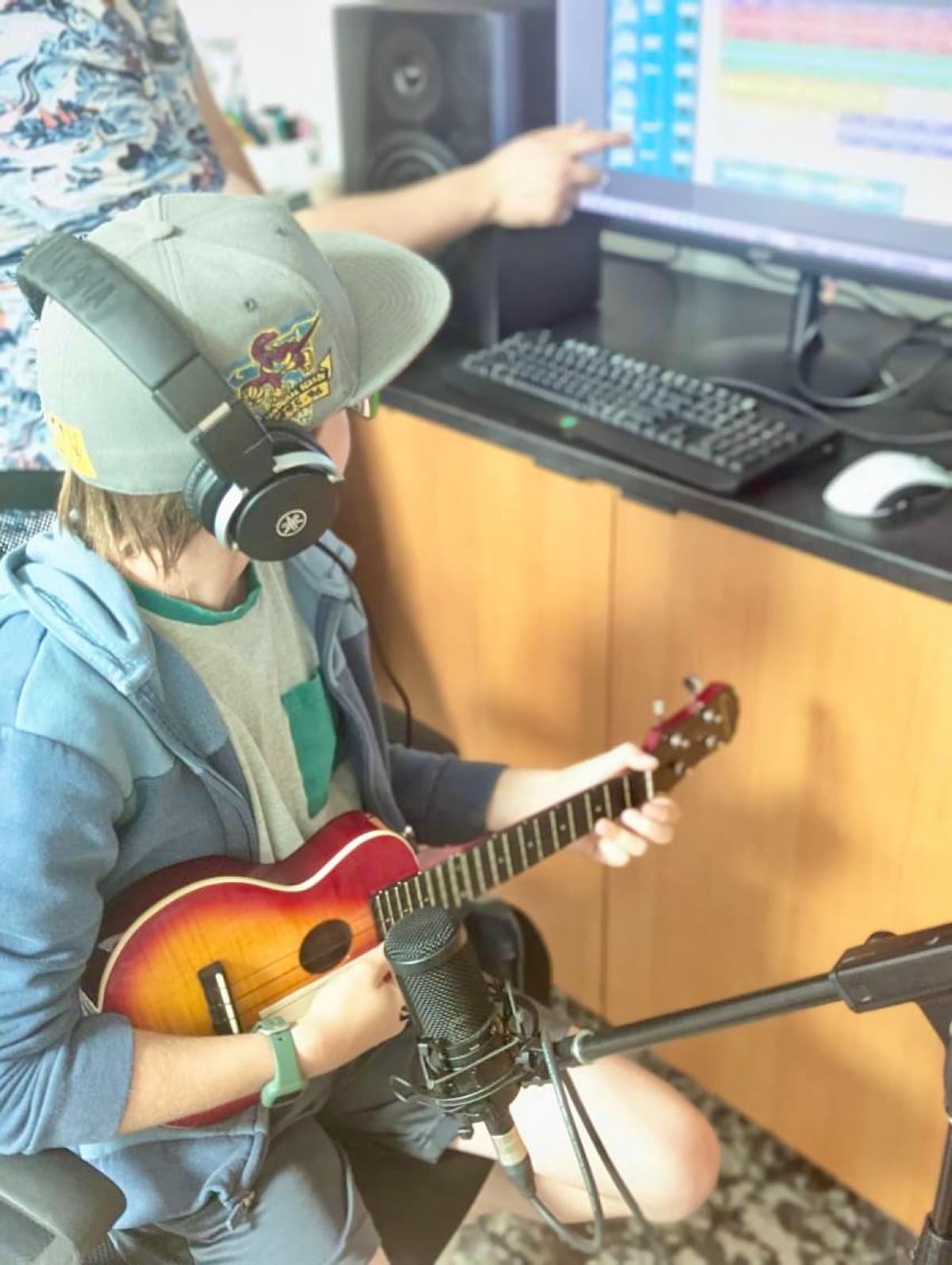 My son wearing headphones and playing guitar in front of a microphone and recording software