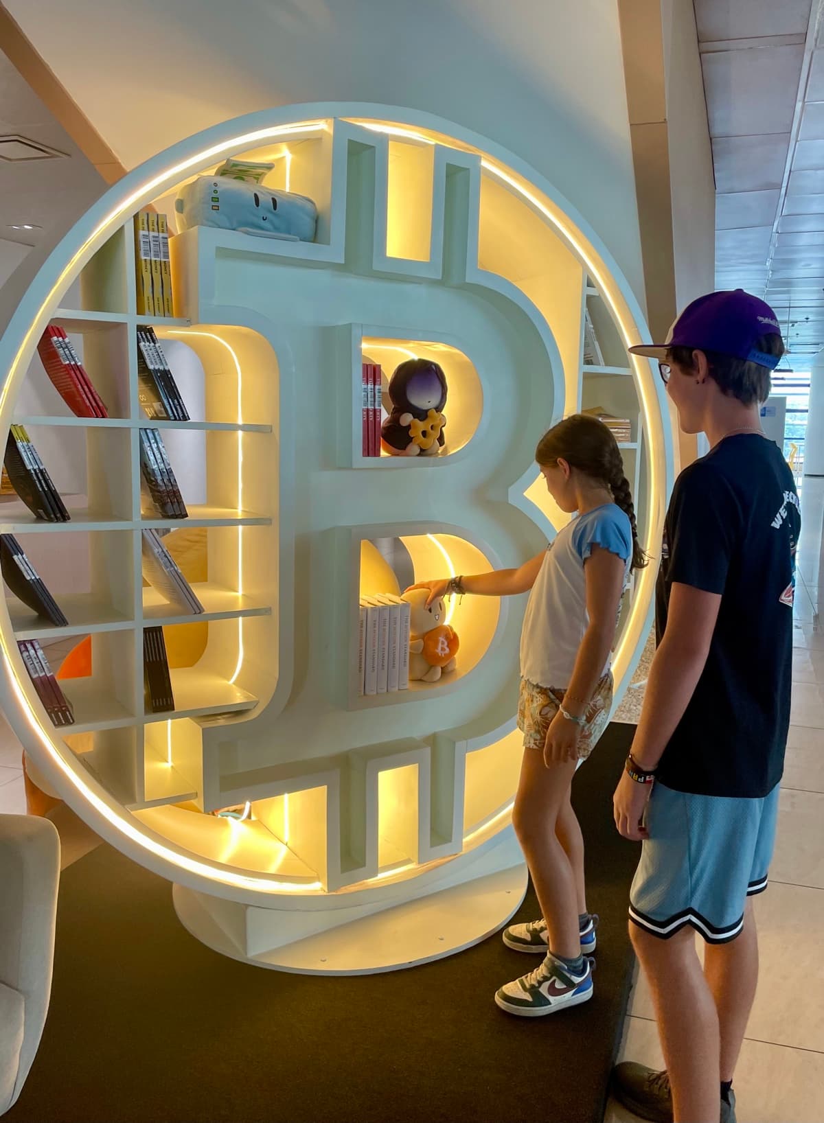 Zach and Julia browsing books inside a giant Bitcoin-shaped bookshelf at the El Salvador national library