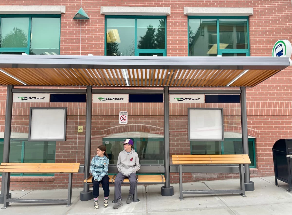 Zach and Julia sitting together at a city bus stop, waiting for the bus on their own