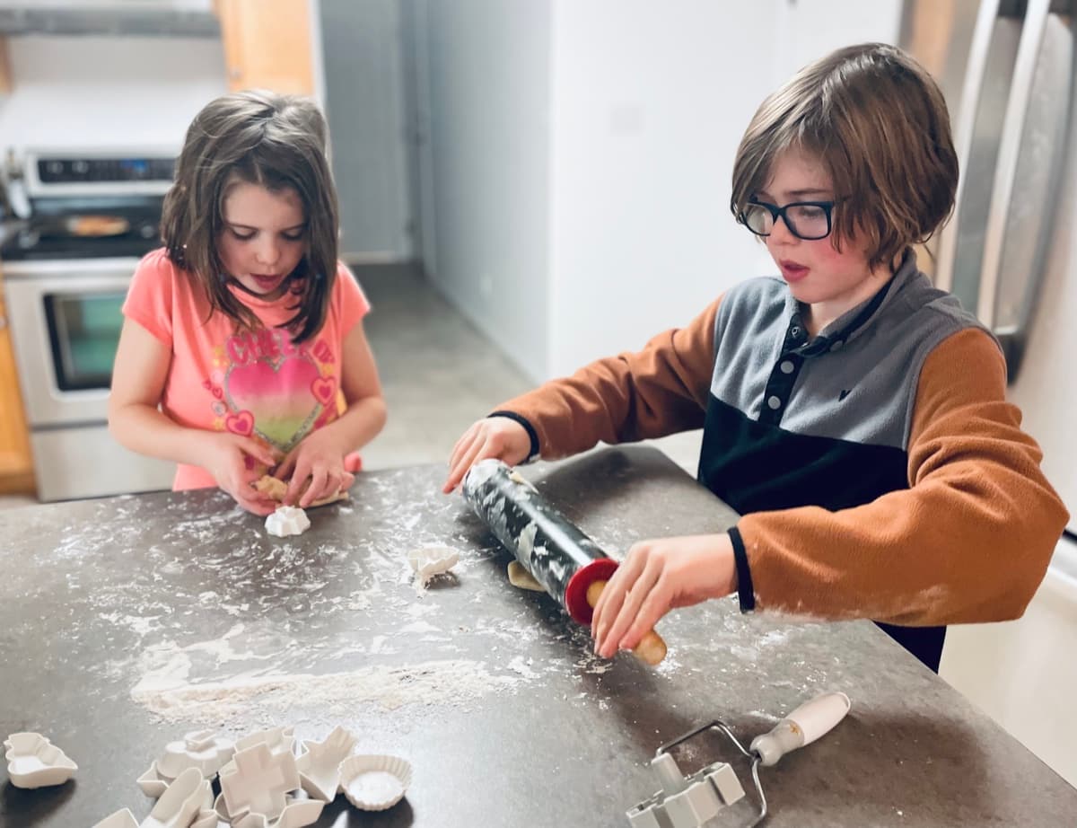 Both kids rolling out cookie dough together at the kitchen counter, real-world learning in action