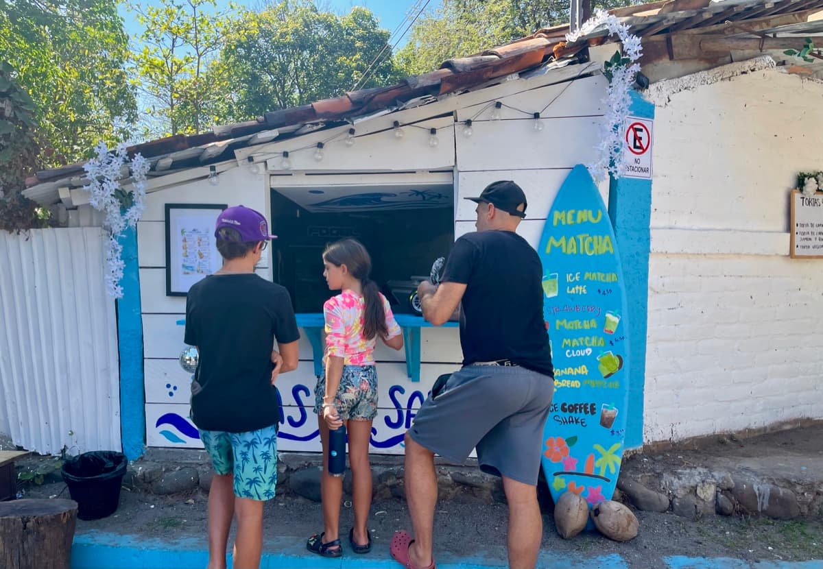 Zach and Julia ordering at a matcha stand in El Salvador, reading a hand-painted menu with prices in USD