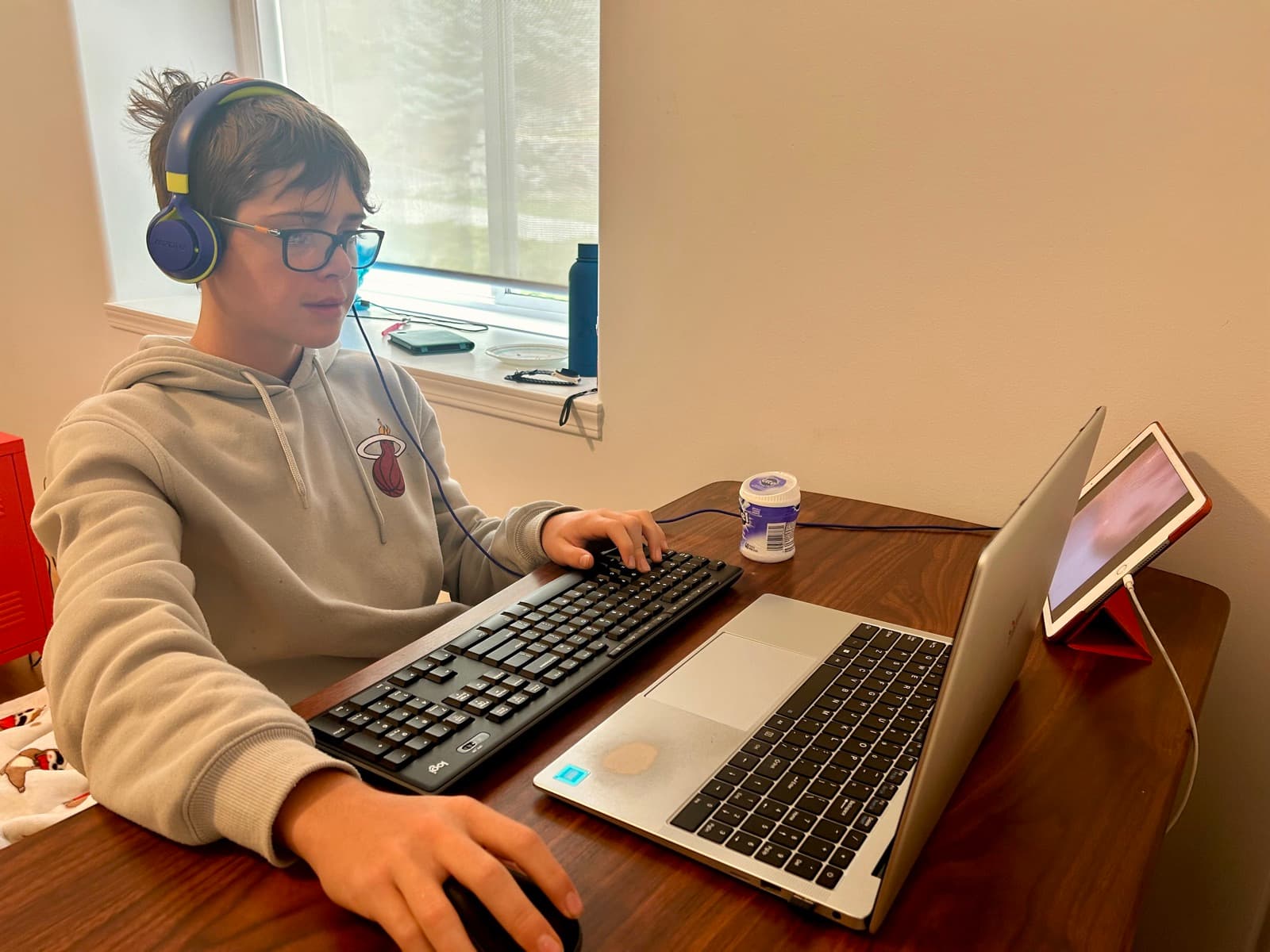 Zach at his desk in headphones and glasses, focused at his laptop with an external keyboard, creating, not passively scrolling