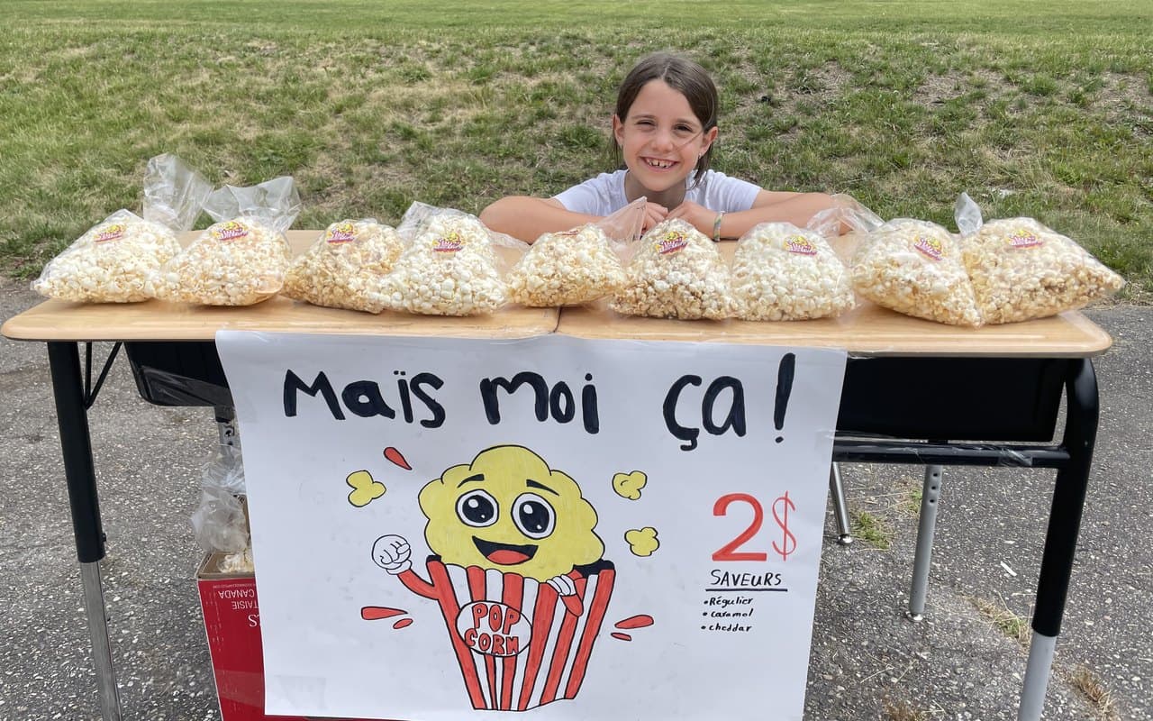 A girl running her own popcorn stand with a hand-painted sign and pricing, a kid business taken from idea to real sales