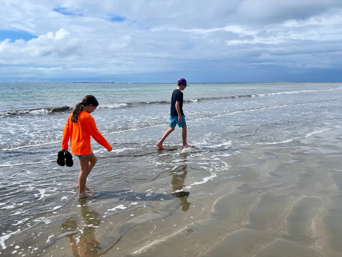 My son and daughter walking side by side through the waves on a quiet beach