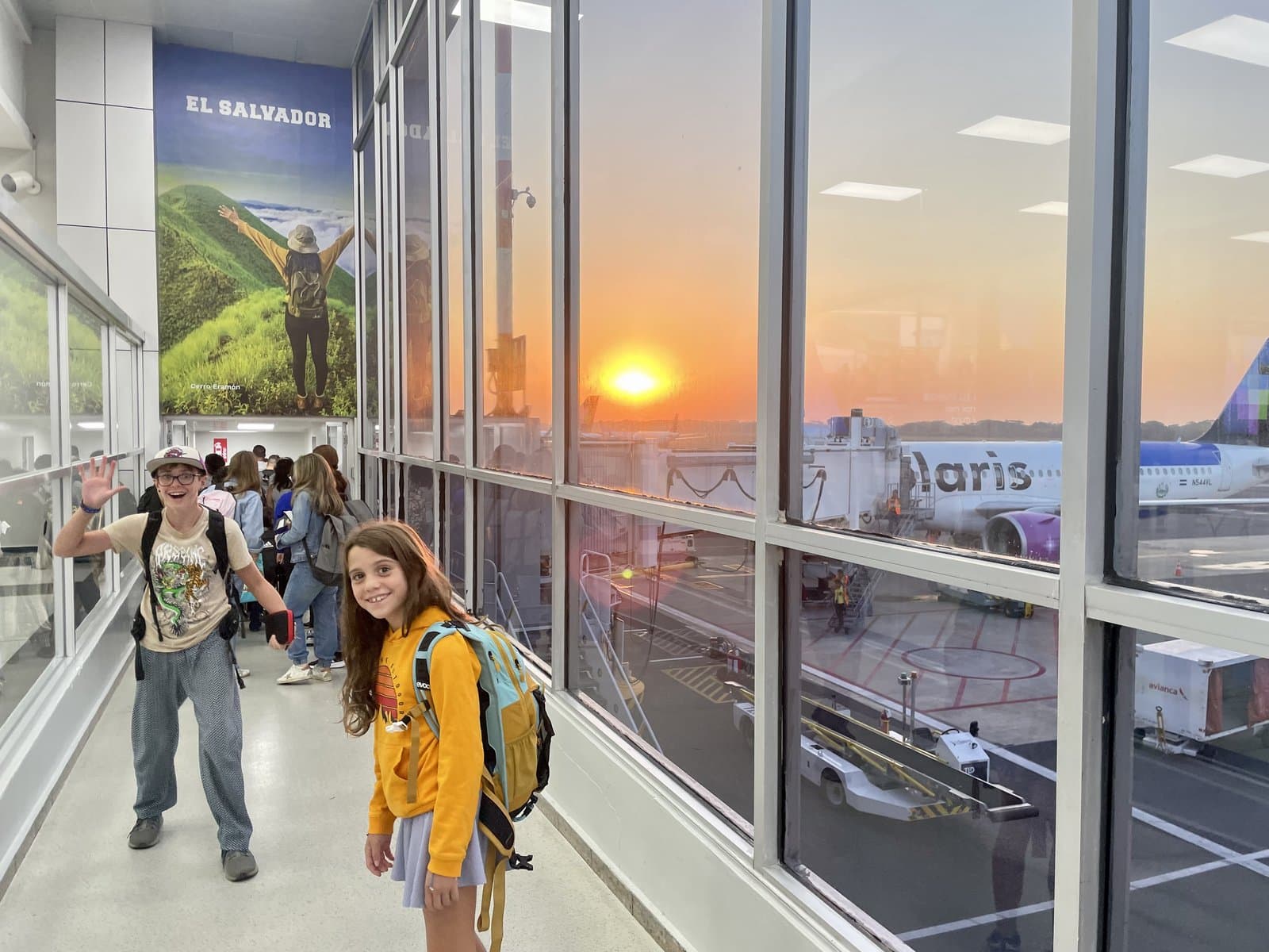 Zach and Julia with backpacks at the airport, sunset glowing through the windows, the start of a new chapter