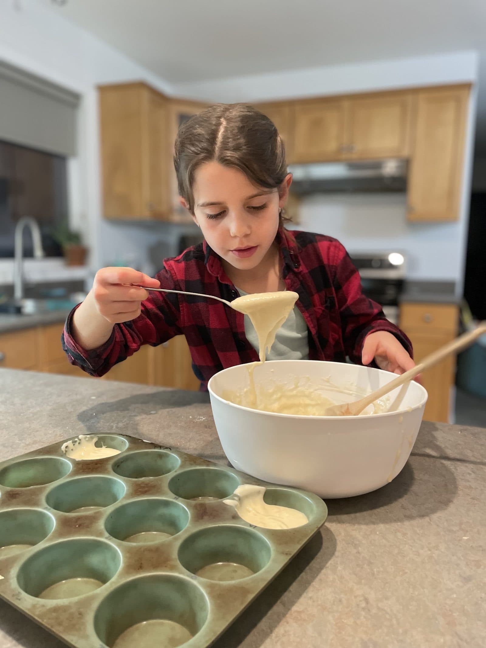 Kid focused on pouring batter into a muffin tin in a sunny kitchen, real measurement and ratios happening