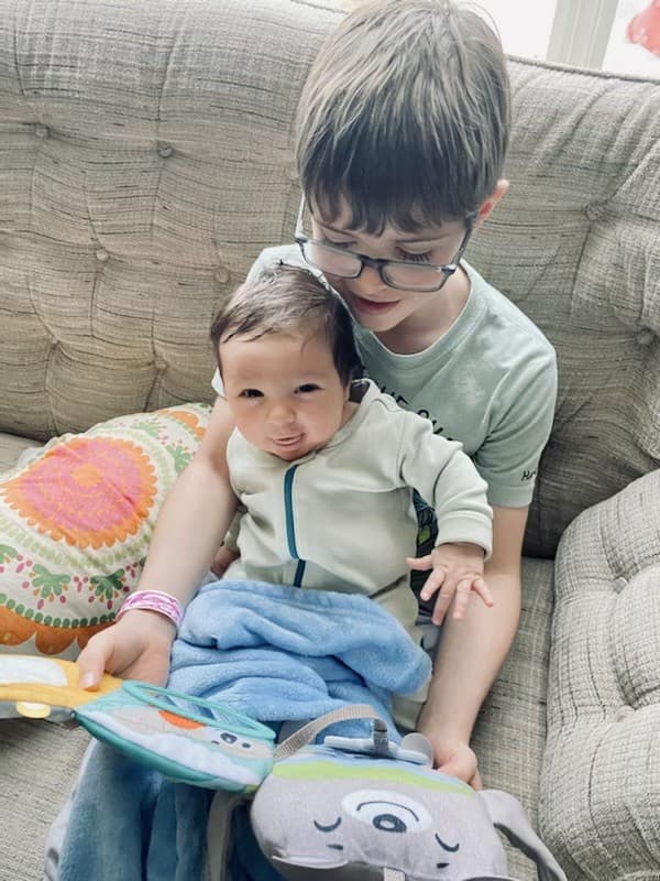 An older child gently holding a baby on the couch and showing them a soft book, an unposed moment of care