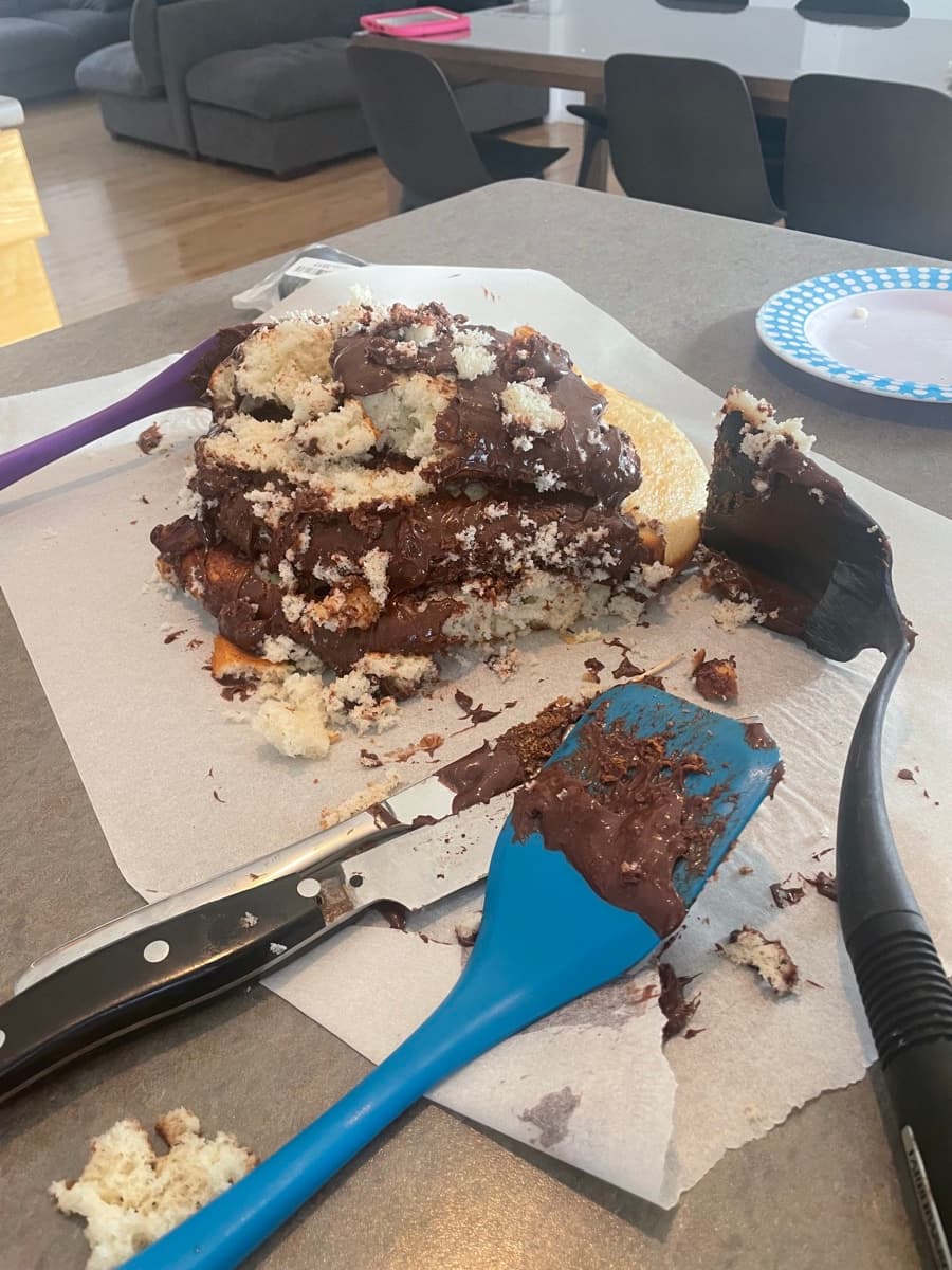 A messy, crumbled chocolate cake with frosting everywhere on the counter
